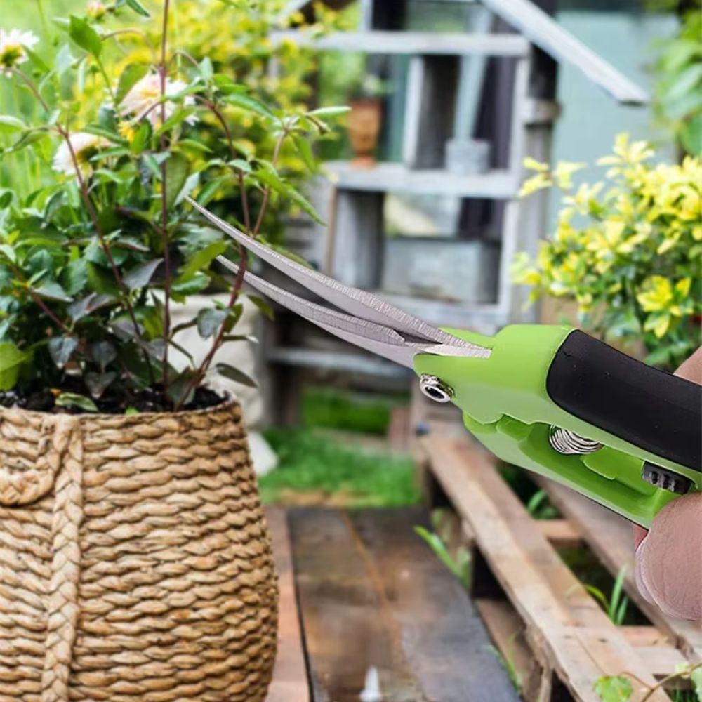 Main en train de tenir un sécateur vert, taillant une plante à l'intérieur d'un jardin