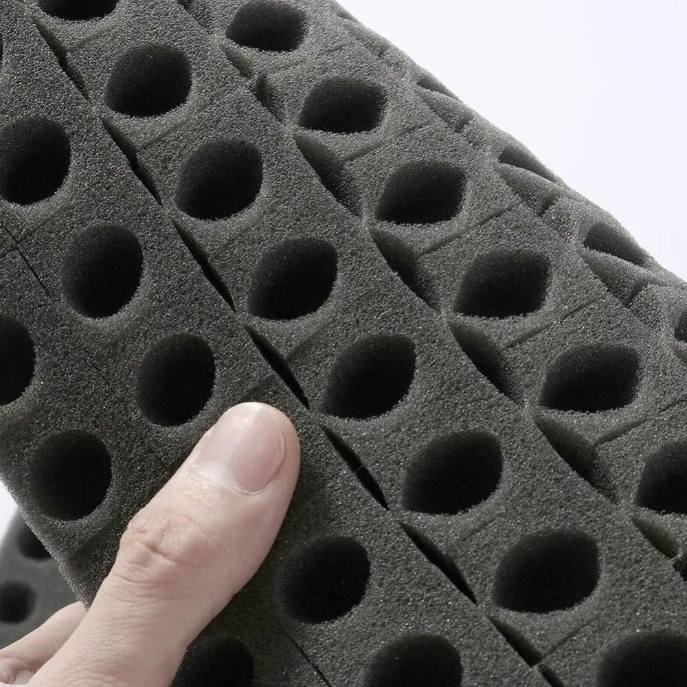 Éponge noire avec des trous ronds, texture douce, tenue en main, fond neutre et clair