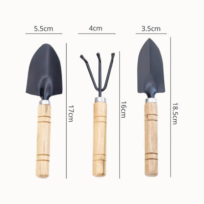 Trois outils de jardinage en métal noir avec des manches en bois, sur fond clair et uniforme