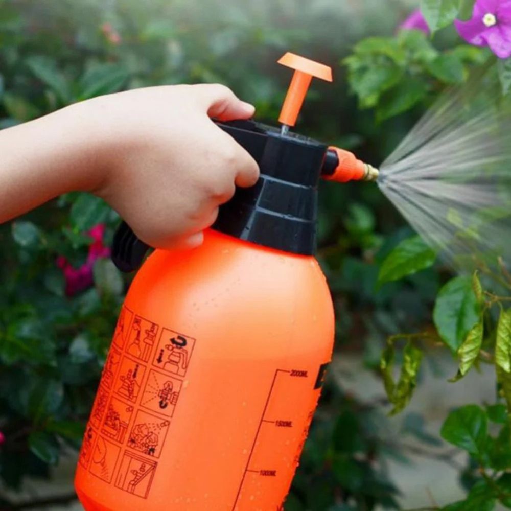 Main tenant un pulvérisateur à pression orange, arrosant des plantes avec une buse réglable