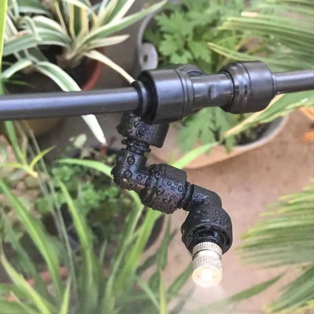 Raccord rapide en T noir en plastique, connecté à des tuyaux et entouré de plantes vertes