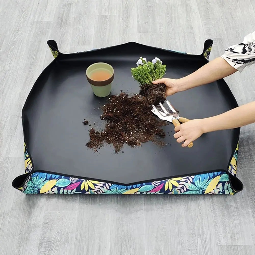 Tapis de rempotage noir avec motifs colorés, pot de terre et plante en cours de rempotage
