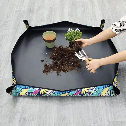 Tapis de rempotage noir avec motifs colorés, pot de terre et plante en cours de rempotage
